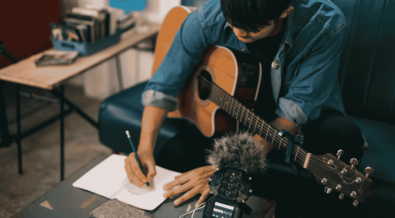 A male songwriter scribbling lyrics to a melody recorded from a wireless microphone